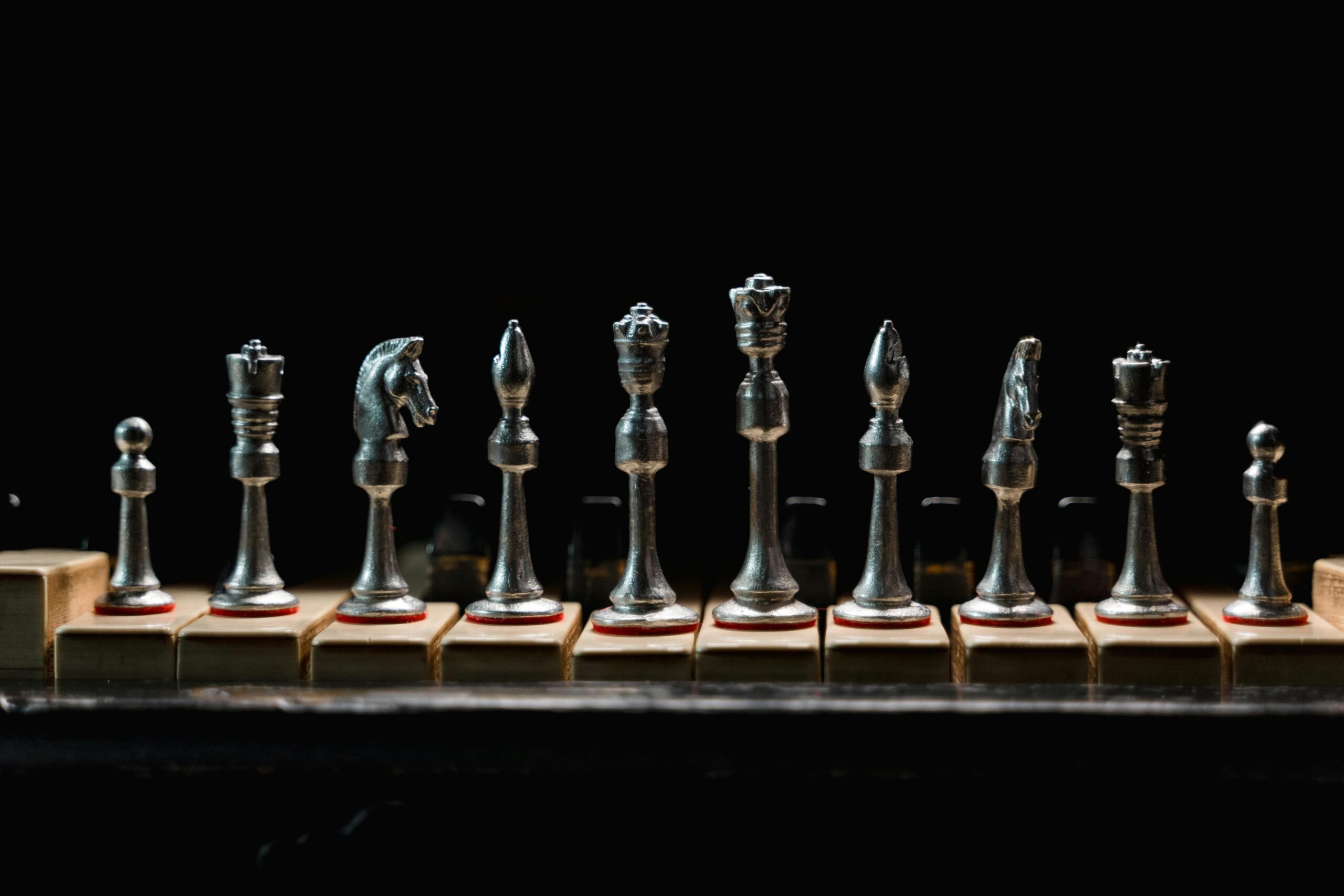 A row of elegant metal chess pieces displayed on wooden blocks against a dark background.