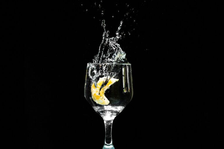 Close-up shot of a lemon slice splashing into a glass of water against a black background.